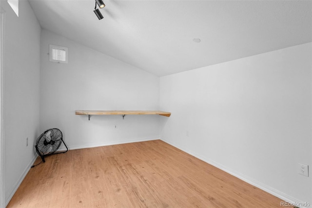empty room with light wood-style flooring, lofted ceiling, and baseboards