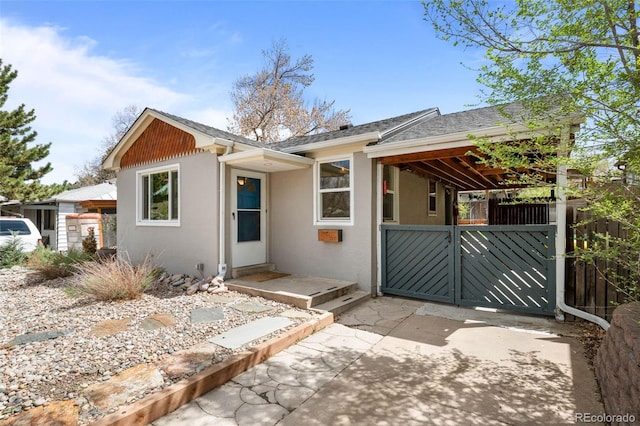 view of front of home featuring a gate, stucco siding, a shingled roof, and fence