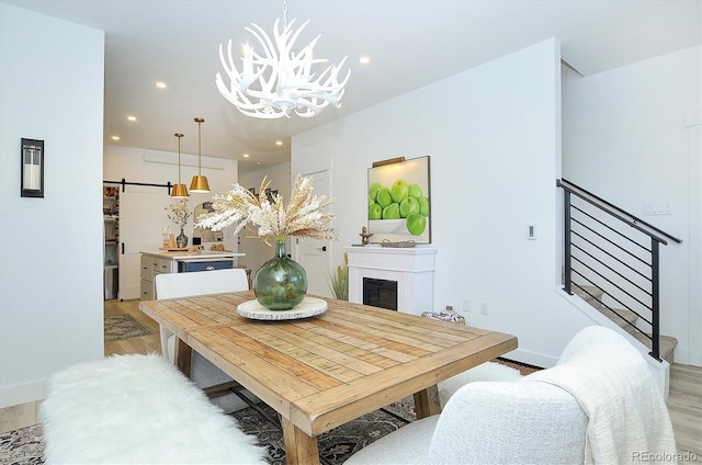 dining space with a barn door, a notable chandelier, and light wood-type flooring