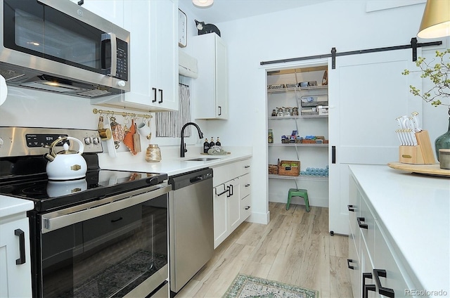 kitchen featuring white cabinetry, sink, stainless steel appliances, a barn door, and light hardwood / wood-style flooring