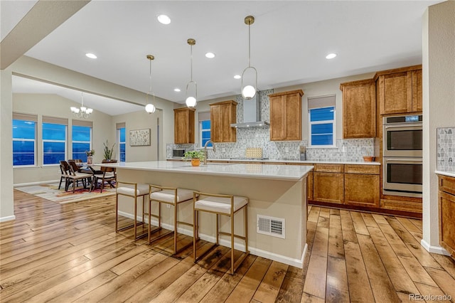 2775 Morningbird Ln, Castle Rock, CO 80109 - kitchen featuring double oven, brown cabinetry, light wood-style floors, wall chimney range hood, and tasteful backsplash