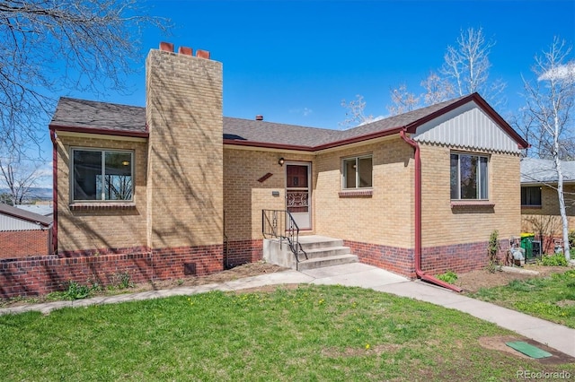 view of front of house featuring a chimney, a front lawn, brick siding, and a shingled roof