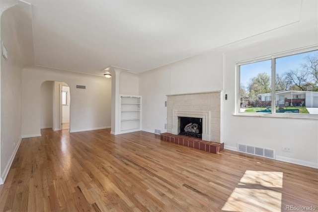 unfurnished living room with arched walkways, wood finished floors, visible vents, and a wealth of natural light