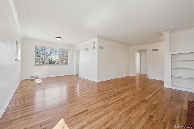 unfurnished living room with light wood-type flooring, arched walkways, built in features, baseboards, and visible vents