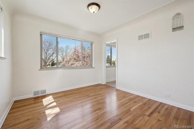 empty room featuring baseboards, wood finished floors, and visible vents