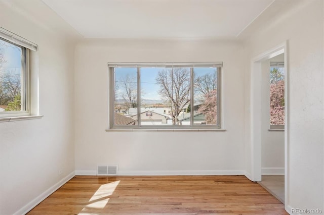 spare room with baseboards, wood finished floors, visible vents, and a wealth of natural light