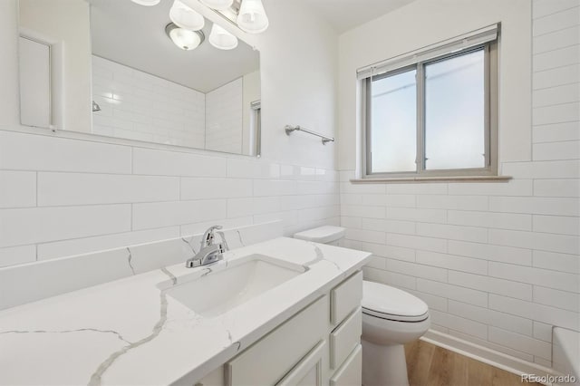 bathroom featuring toilet, vanity, wood finished floors, and tile walls