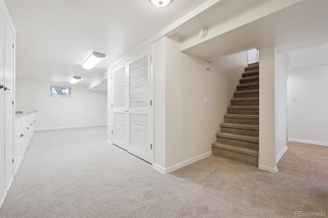 basement featuring baseboards, carpet floors, and stairway