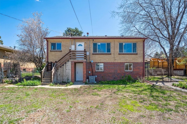 view of front of home with fence, brick siding, central air condition unit, and stairway