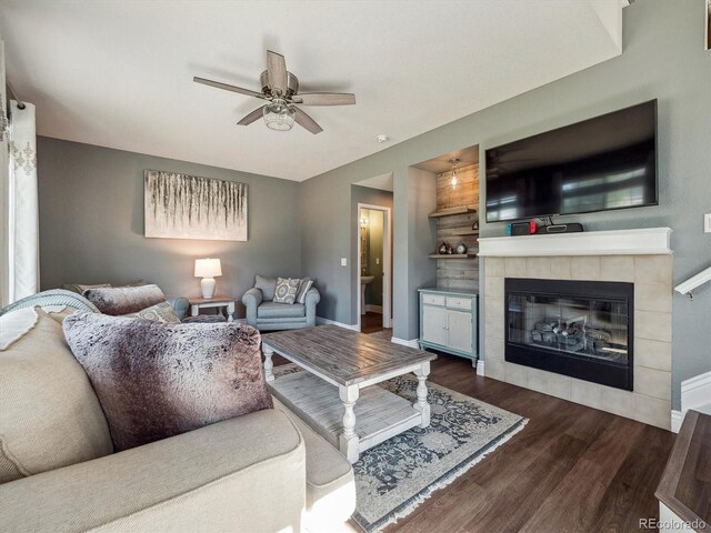 living area featuring dark wood-type flooring, a ceiling fan, baseboards, and a fireplace
