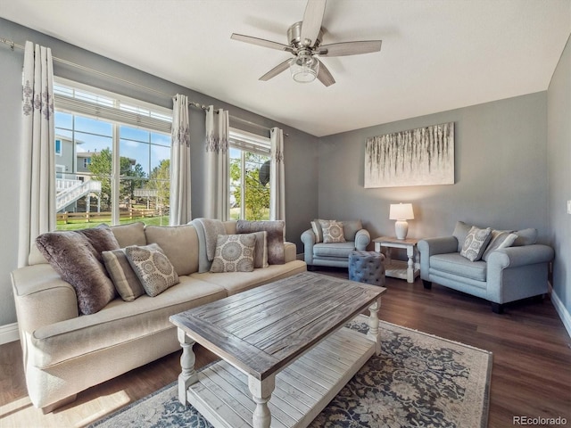 living area featuring a ceiling fan, dark wood finished floors, and baseboards