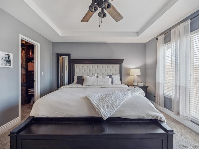 carpeted bedroom with a tray ceiling, baseboards, and a ceiling fan