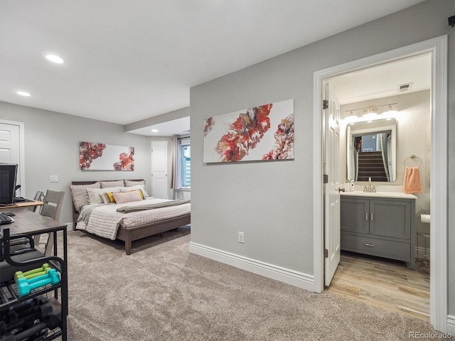 bedroom with baseboards, recessed lighting, light carpet, ensuite bathroom, and a sink