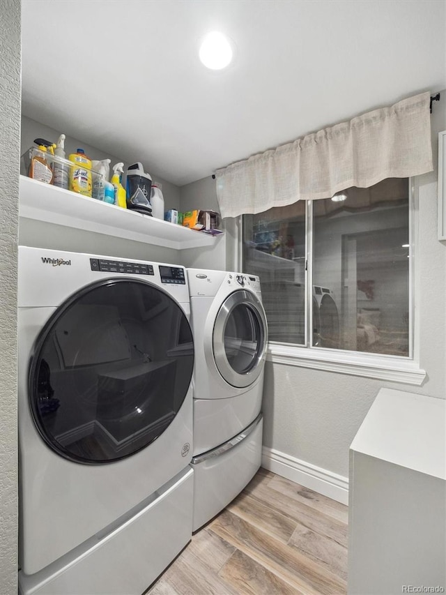 laundry area with light wood-type flooring, washing machine and dryer, and baseboards