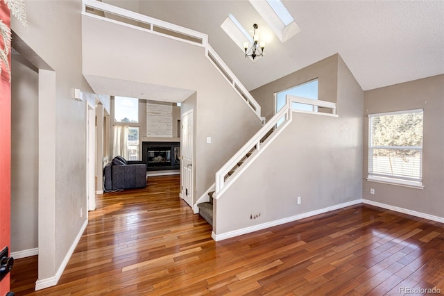 unfurnished living room featuring a skylight, high vaulted ceiling, a healthy amount of sunlight, and hardwood / wood-style flooring