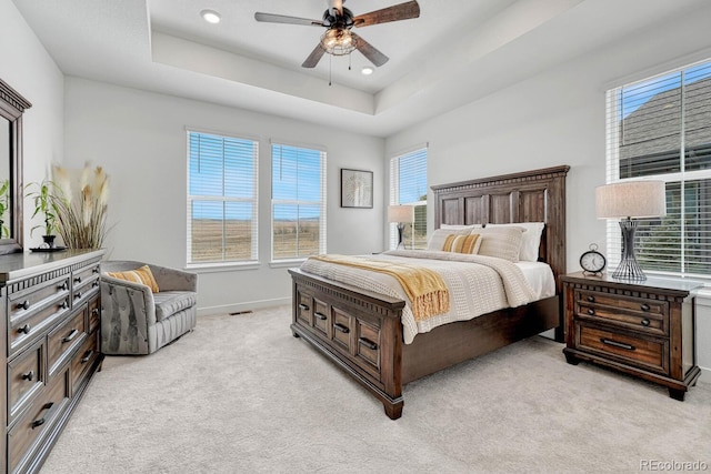 bedroom featuring light colored carpet, a raised ceiling, and ceiling fan