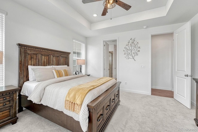 bedroom with a raised ceiling, light colored carpet, and ceiling fan