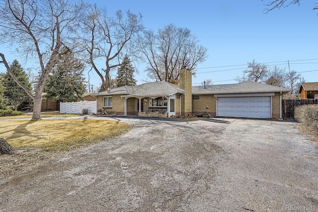 ranch-style house with brick siding, a chimney, driveway, and fence