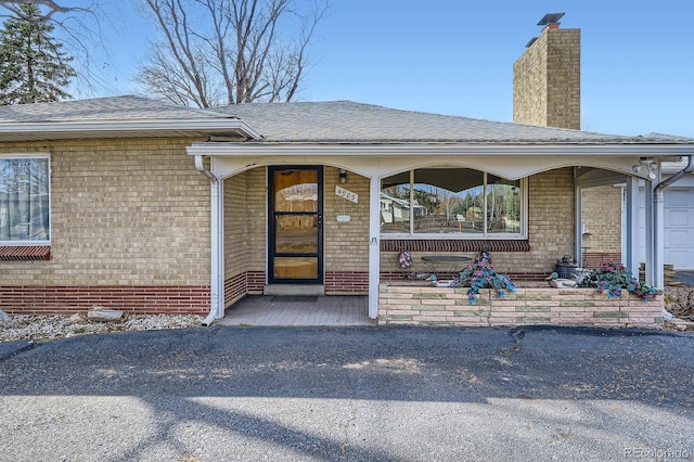 entrance to property with brick siding, a porch, a chimney, and roof with shingles