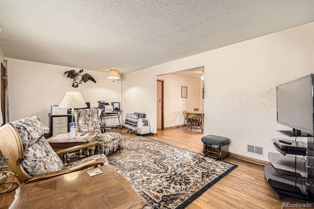 living area featuring visible vents, light wood-style flooring, a textured ceiling, and baseboards