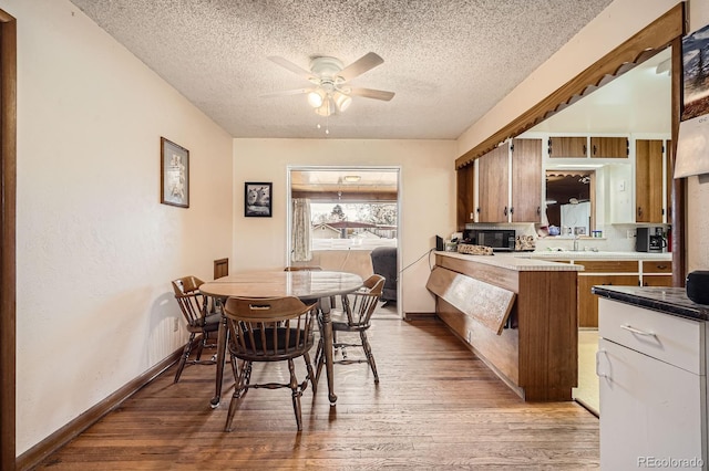 dining room with a ceiling fan, light wood-style floors, baseboards, and a textured ceiling