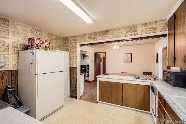 kitchen featuring a peninsula, freestanding refrigerator, light countertops, black microwave, and brown cabinets