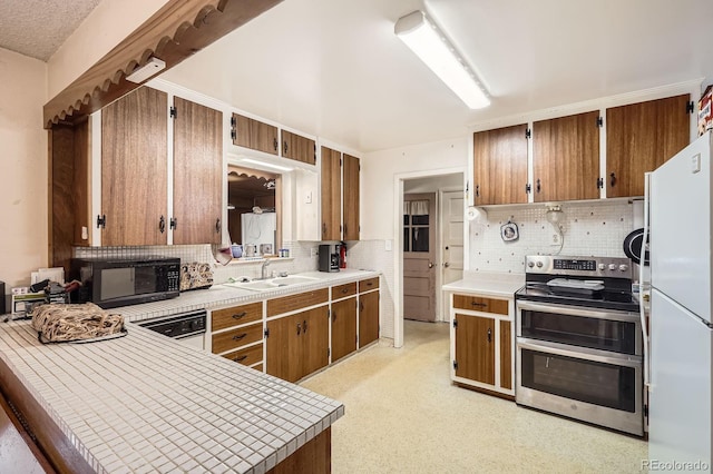 kitchen featuring a sink, freestanding refrigerator, black microwave, light countertops, and range with two ovens