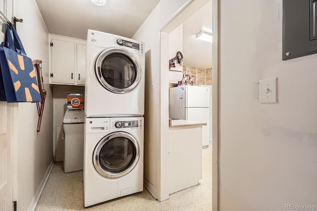 clothes washing area featuring electric panel, baseboards, cabinet space, and stacked washer / dryer