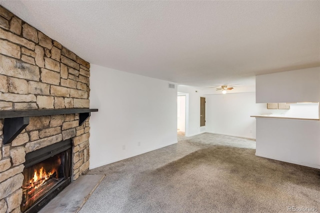 unfurnished living room with a stone fireplace, carpet flooring, ceiling fan, and visible vents