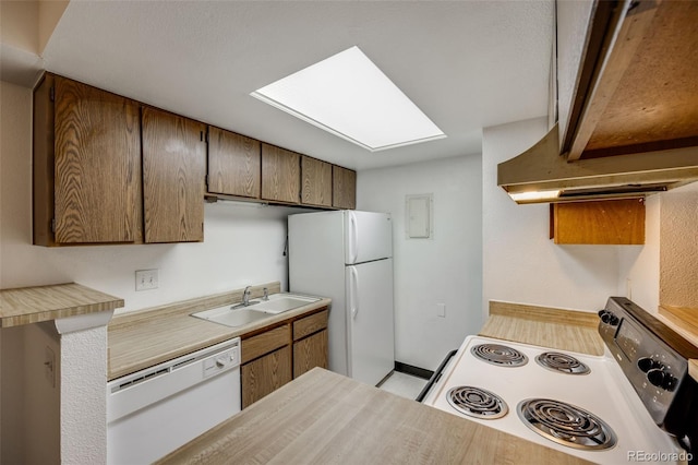 kitchen with white appliances, baseboards, light countertops, a sink, and a skylight
