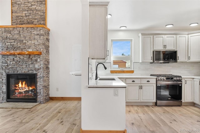 kitchen featuring stainless steel appliances, a sink, light countertops, light wood finished floors, and tasteful backsplash