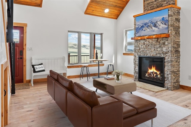 living area featuring light wood-style floors, baseboards, high vaulted ceiling, and a stone fireplace