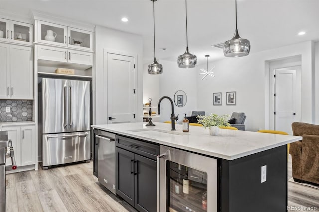 kitchen with sink, white cabinetry, wine cooler, stainless steel refrigerator, and a center island with sink