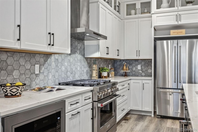 kitchen featuring white cabinetry, light stone counters, wall chimney exhaust hood, and appliances with stainless steel finishes