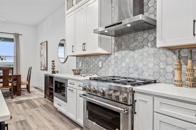 kitchen with stainless steel appliances, wall chimney range hood, light hardwood / wood-style flooring, and white cabinets