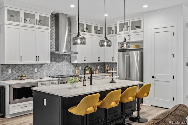 kitchen featuring white cabinets, a center island with sink, appliances with stainless steel finishes, light stone countertops, and wall chimney exhaust hood