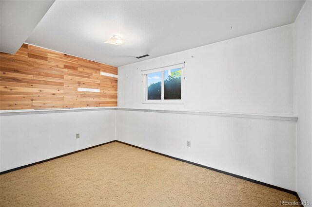 carpeted empty room featuring wood walls