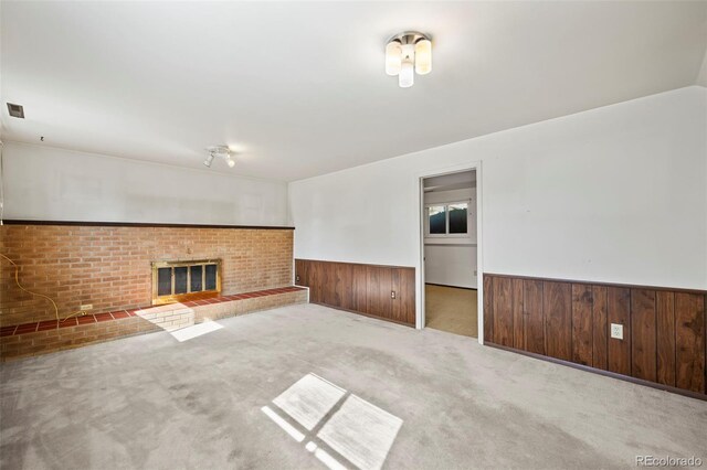 empty room with light carpet, wooden walls, and a fireplace