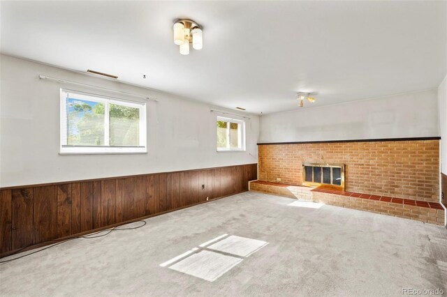 unfurnished living room with light carpet, wooden walls, and a brick fireplace