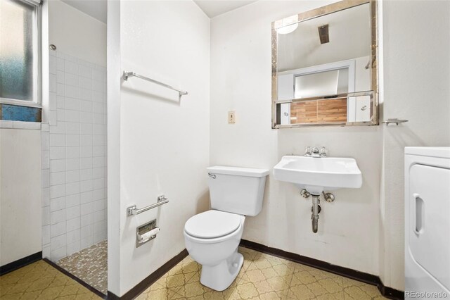 bathroom with tiled shower, toilet, washer / dryer, and sink