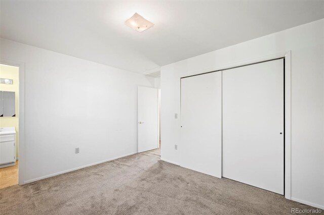 unfurnished bedroom featuring light carpet, a closet, and ensuite bathroom