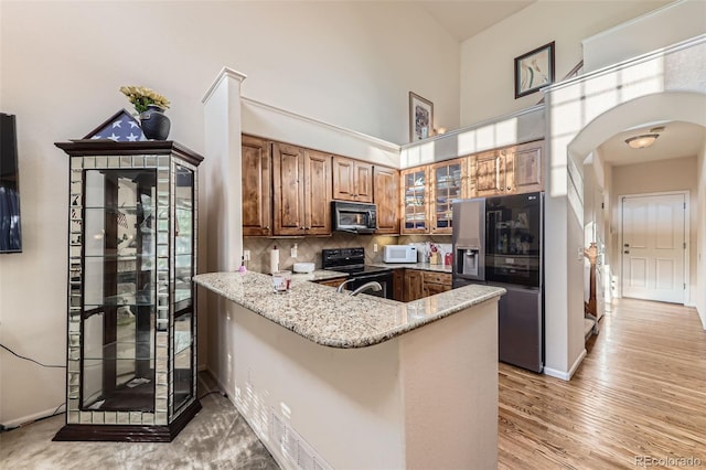15501 E 112th Ave Unit 28E, Commerce City, CO 80022 - kitchen featuring black appliances, arched walkways, brown cabinetry, a peninsula, and glass insert cabinets