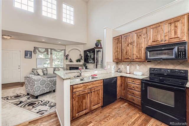 15501 E 112th Ave Unit 28E, Commerce City, CO 80022 - kitchen featuring black appliances, a sink, a fireplace, light wood finished floors, and a towering ceiling