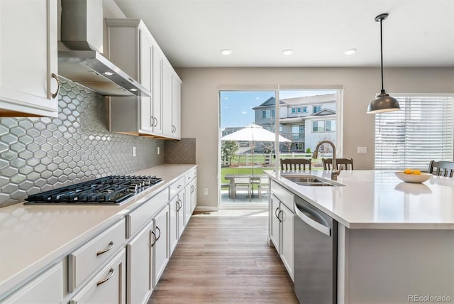 kitchen with wall chimney range hood, a sink, light countertops, stainless steel appliances, and light wood-type flooring
