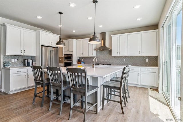 kitchen featuring decorative backsplash, light wood-type flooring, light countertops, wall chimney exhaust hood, and white cabinets