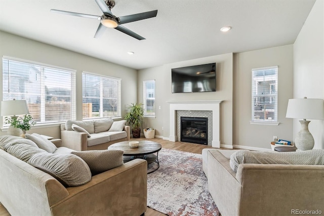 living room with baseboards, light wood-style flooring, a glass covered fireplace, and a healthy amount of sunlight