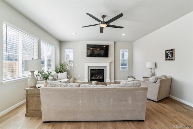 living area featuring a glass covered fireplace, baseboards, ceiling fan, recessed lighting, and light wood-type flooring