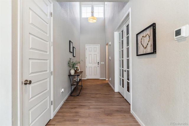 entryway featuring baseboards, wood finished floors, and a towering ceiling