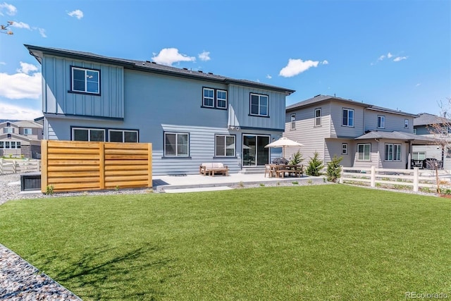rear view of property featuring a lawn, board and batten siding, a patio area, and fence