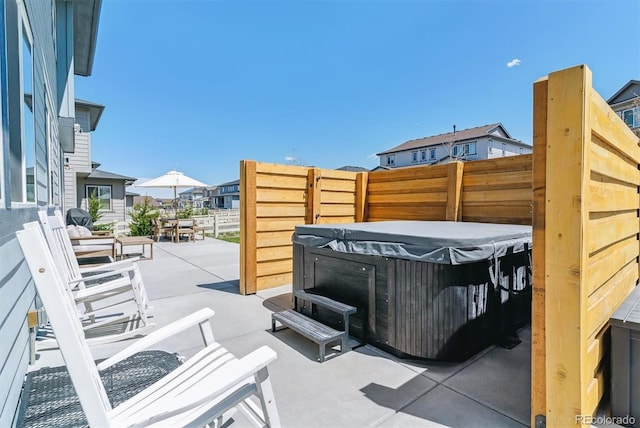 view of patio / terrace with a hot tub, fence, and a residential view